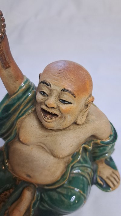 Antica statua di Buddha in terracotta con un braccio sollevato