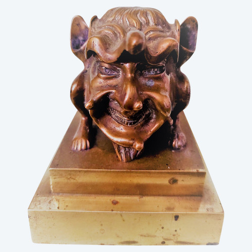 Old inkwell in gilded bronze on a base with the head of a laughing monster