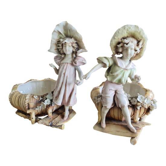 Bohemian-style porcelain figurines of children with shallow bowls, decorated with applique flowers dating to around 1900