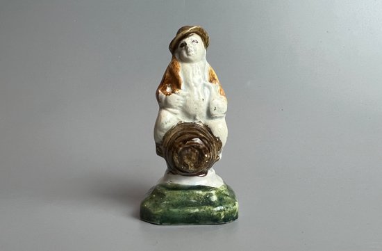 A c1790 Staffordshire pratt coloured pearlware toper figure seated on a barrel.