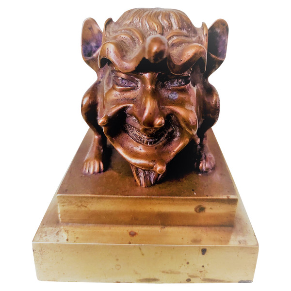 Old inkwell in gilded bronze on a base with the head of a laughing monster