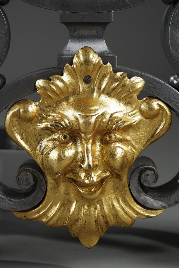 Paire de landiers en fer forgé à décor feuillagé, masque et volutes